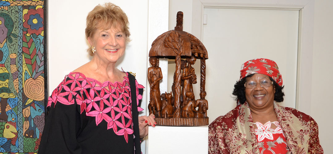 Two women standing on either side of an African wooden sculpture
