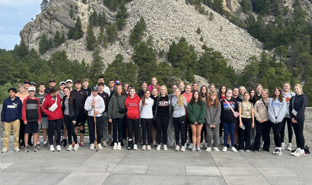 Large group of students posing in two rows at Mount Rushmore.