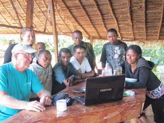 Man sitting at an outdoor table looking at a laptop with eight African children.