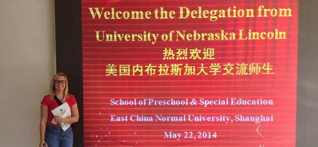 College student standing in front of a large wall banner that reads "Welcome the Delegation from University of Nebraska  Lincoln"