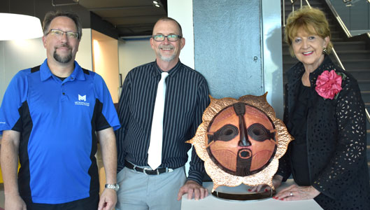 Three people standing next to display of African mask