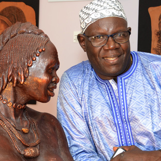 African man sitting next to a bronze statue of an African women wearing braids
