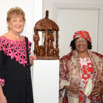 Two woman standing on either side of an African wooden sculpture