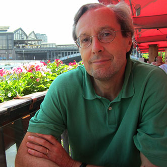 Man in green shirt sitting in outdoor cafe with a red umbrella behind him and flowers