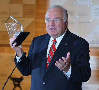 J. Joe Ricketts holding glass award and speaking