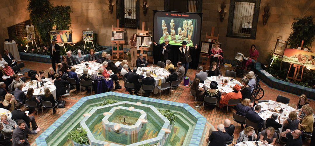 Auctioneers at a gala event presiding over several tables of guests