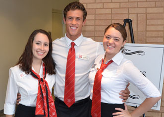 Three students standing side by side smiling wearing white shirts and red ties